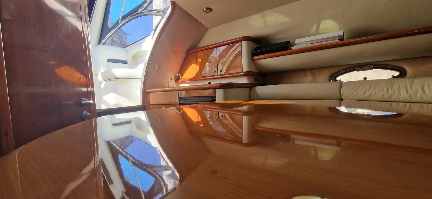 Interior of a luxury yacht featuring polished wooden surfaces, a small kitchenette area, and natural light streaming through windows.